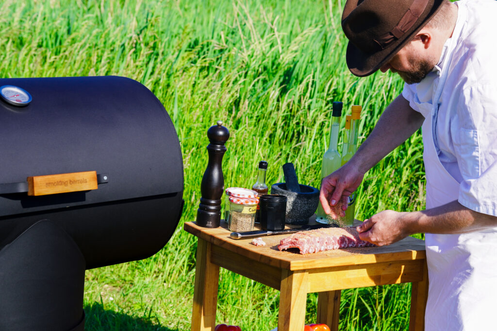 Een chef verspreidt een zelfgemaakte BBQ rub over spareribs met zijn handen voor een gelijkmatige bedekking.