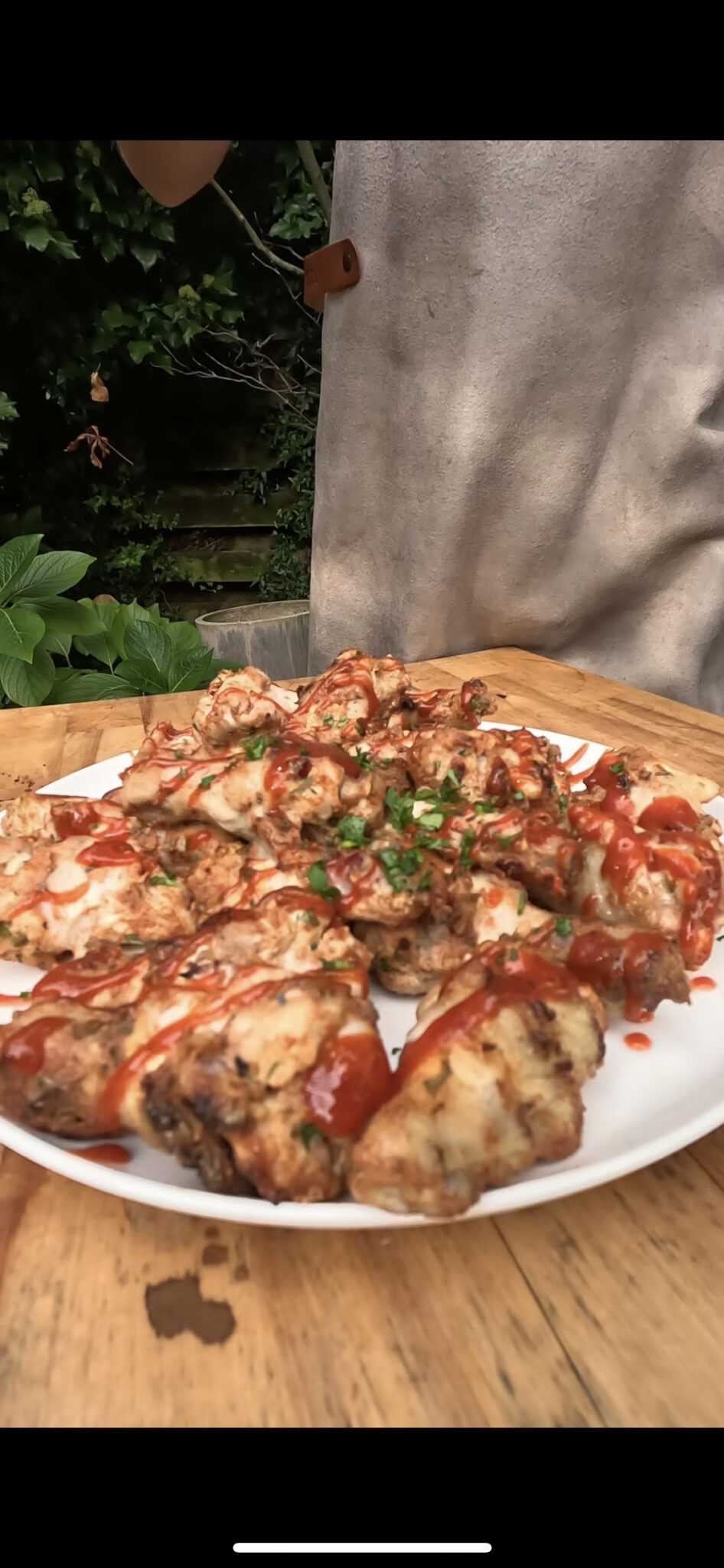 Foto van een bord kippenvleugels met srirachasaus en peterselie eroverheen: