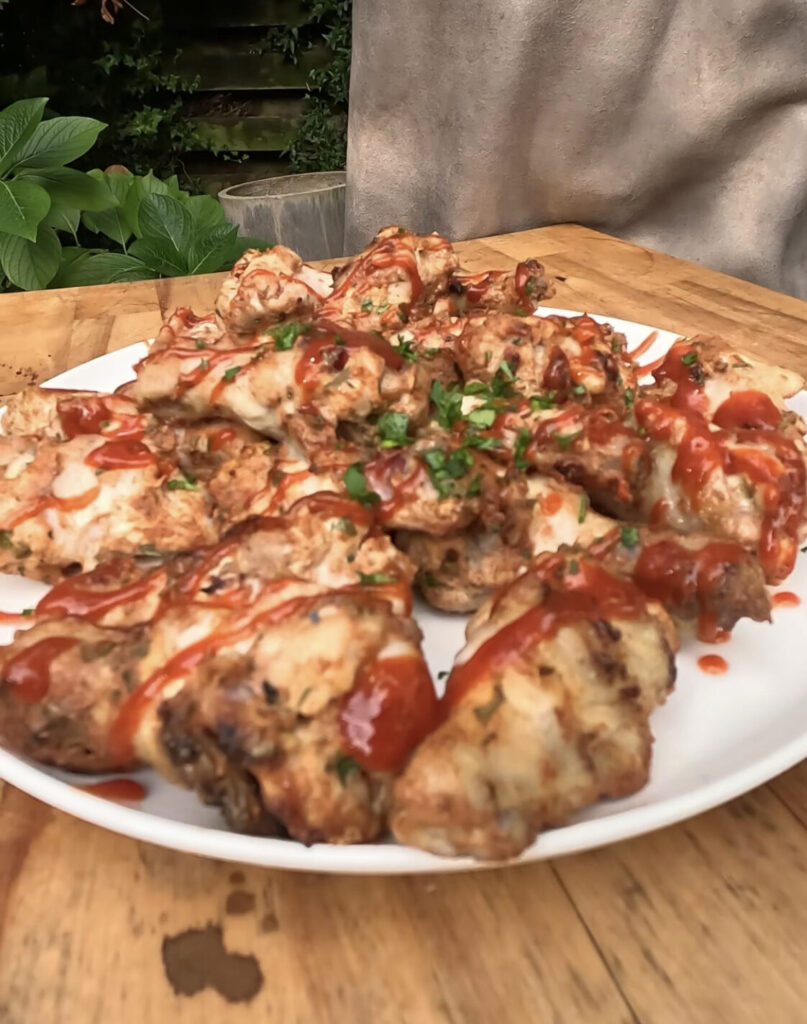 Foto van een bord kippenvleugels met srirachasaus en peterselie eroverheen: